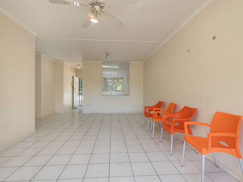 Spacious open-plan living area featuring neutral ceramic floor tiles, a ceiling fan, and a convenient pass-through window connecting to the kitchen.