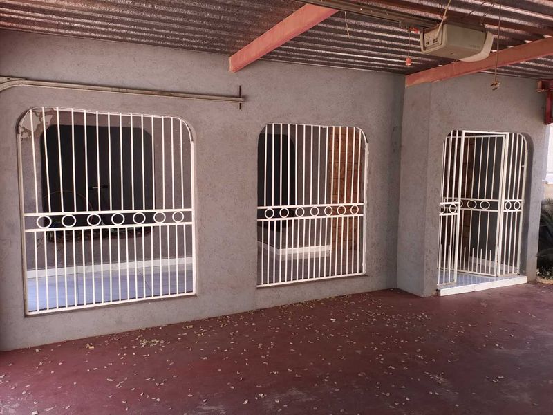 A covered outdoor patio area featuring security gates, corrugated metal roofing, and concrete flooring, suitable for renovation or outdoor living space enhancement.