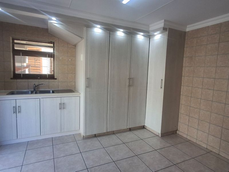 A clean and functional scullery area featuring ample built-in cabinetry, a stainless steel sink, and neutral tiled finishes throughout.