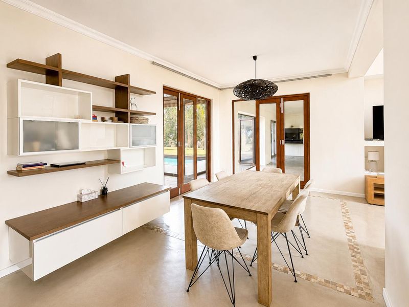 Bright dining room featuring polished concrete floors with decorative inlay, built-in wall shelving, and timber-framed glass doors opening to the outdoor pool area.