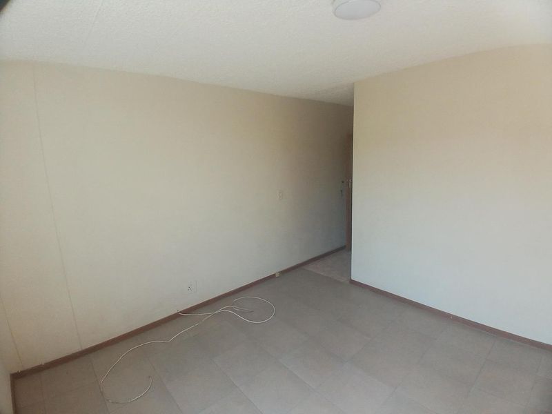 An empty, neutrally painted living area featuring tiled flooring and basic ceiling lighting, offering a blank canvas for potential interior design updates.