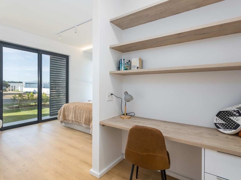 Modern bedroom featuring a built-in desk with floating shelving, light wood-look flooring, and large sliding glass doors providing access to the exterior.