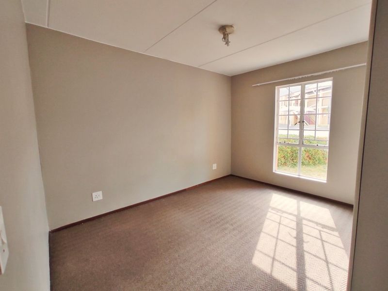 A clean, empty bedroom featuring neutral wall paint, carpeted flooring, and a window with security bars, offering a blank canvas for personalization.