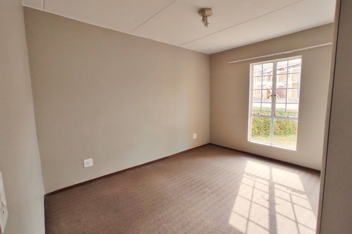 A clean, empty bedroom featuring neutral wall paint, carpeted flooring, and a window with security bars, offering a blank canvas for personalization.