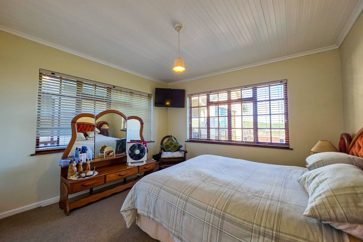 A well-lit bedroom featuring carpeted flooring, tongue and groove ceiling paneling, and large windows with fitted venetian blinds.