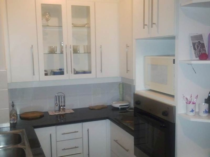 A functional kitchen featuring white cabinetry, black granite countertops, a built-in oven, microwave, and a stainless steel sink with tiled backsplash.