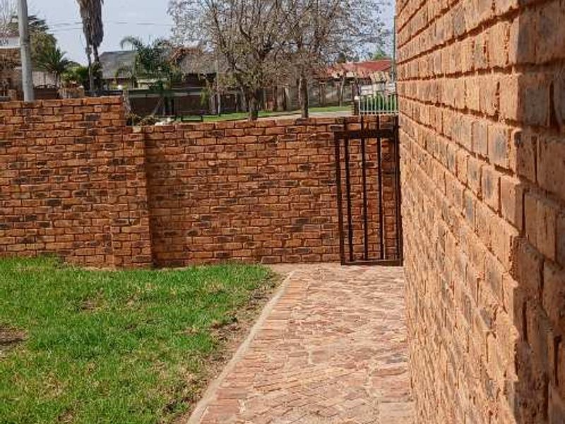 A side view of the property showing a brick exterior wall, cobblestone pathway, and a small metal gate leading to the rear garden area.