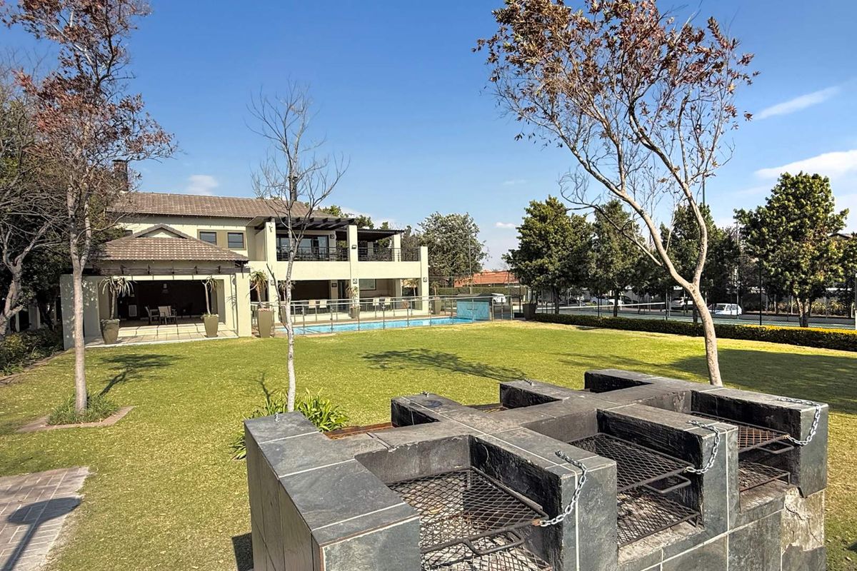 A spacious rear garden featuring a built-in stone braai area, manicured lawn, and a swimming pool set against the rear elevation of the property.