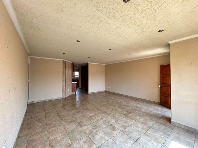 Spacious open-plan living area featuring neutral tiled flooring, recessed downlighting, and a textured ceiling, providing a versatile blank canvas for interior design.