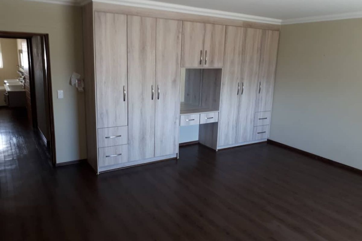 Spacious bedroom featuring modern light wood built-in cupboards with integrated vanity and dark laminate flooring.