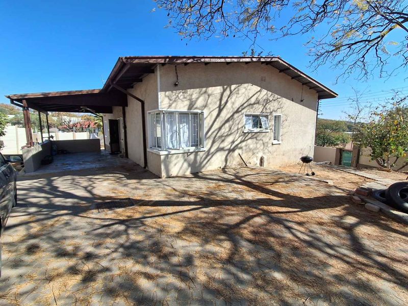 Rear view of the house featuring a covered patio area, paved driveway, and security bars on the windows.