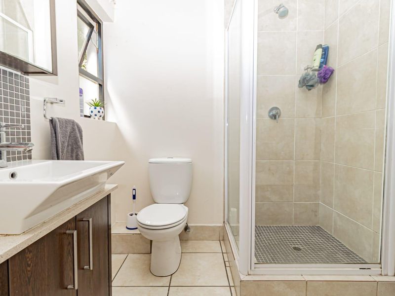 A functional bathroom featuring a vanity with basin, a standard toilet, and a glass-enclosed shower with neutral wall and floor tiling.