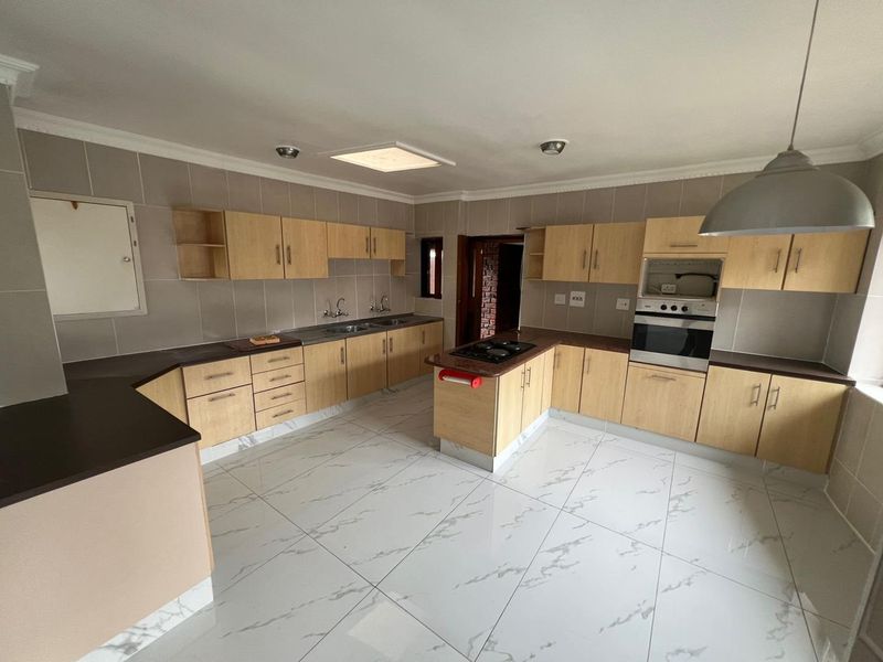 Spacious kitchen featuring light wood cabinetry, dark countertops, built-in oven and hob, and modern marble-look floor tiles.