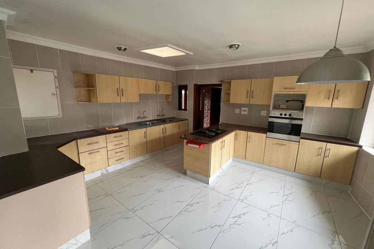 Spacious kitchen featuring light wood cabinetry, dark countertops, built-in oven and hob, and modern marble-look floor tiles.