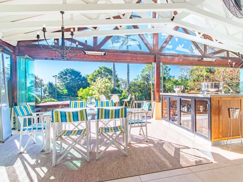 Spacious covered patio featuring exposed timber roof trusses, glass stacker doors for seamless indoor-outdoor flow, and a built-in bar area.