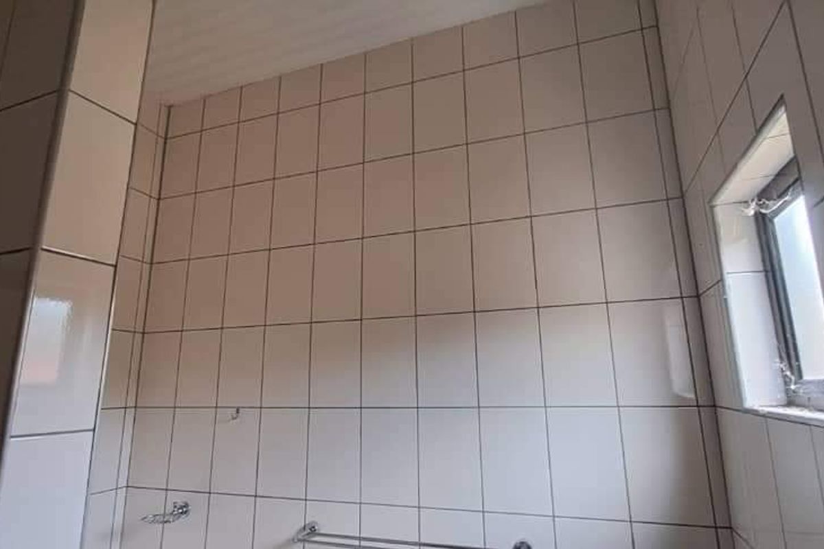 A functional bathroom space featuring full-height wall tiling, a small window for natural light, and fixed chrome towel rails.