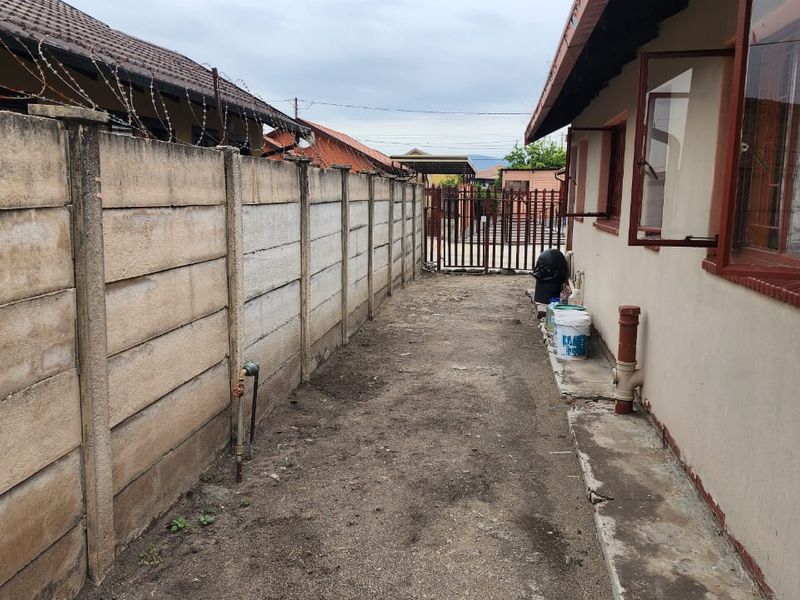 A narrow side yard area featuring a precast concrete boundary wall with security razor wire and an access gate.