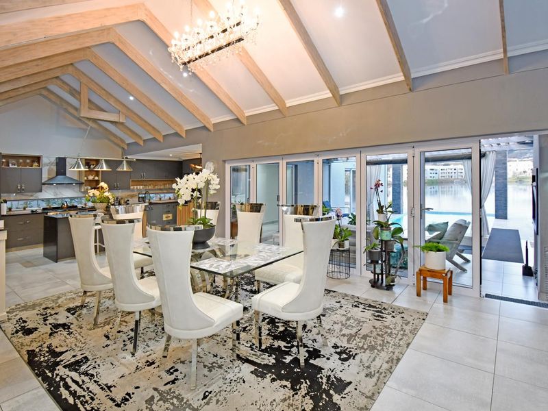 Spacious open-plan dining and kitchen area featuring vaulted ceilings with exposed beams, modern cabinetry, and large bi-fold doors opening to a pool deck.