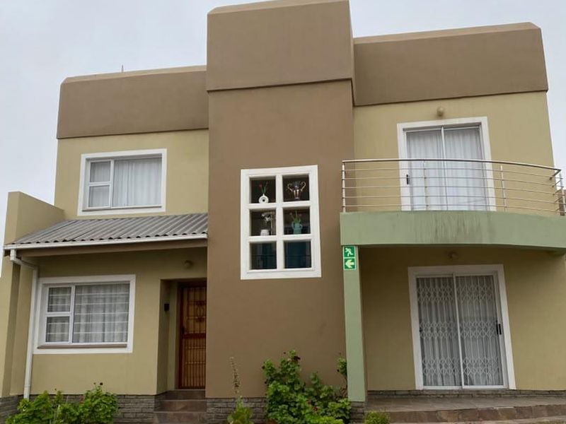 Front elevation of a two-story apartment building featuring a balcony, paved driveway, and modern exterior finishes.