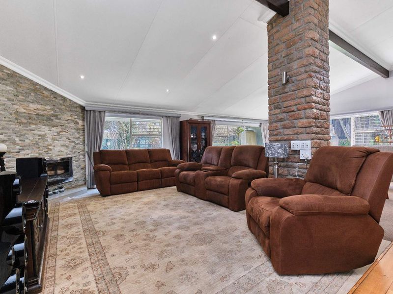 Spacious living room featuring a vaulted ceiling with exposed timber beams, a prominent stone fireplace, and a central exposed brick pillar.