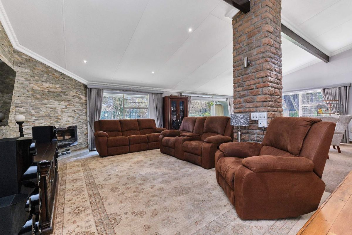 Spacious living room featuring a vaulted ceiling with exposed timber beams, a prominent stone fireplace, and a central exposed brick pillar.