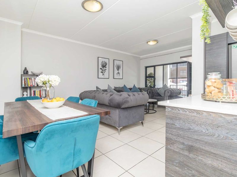 An open-plan living and dining area featuring tiled flooring, modern kitchen cabinetry with stone countertops, and direct access to a balcony.