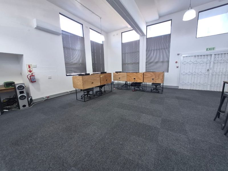 Spacious office area featuring high ceilings, carpeted flooring, large windows with blinds, and a secure entrance gate.