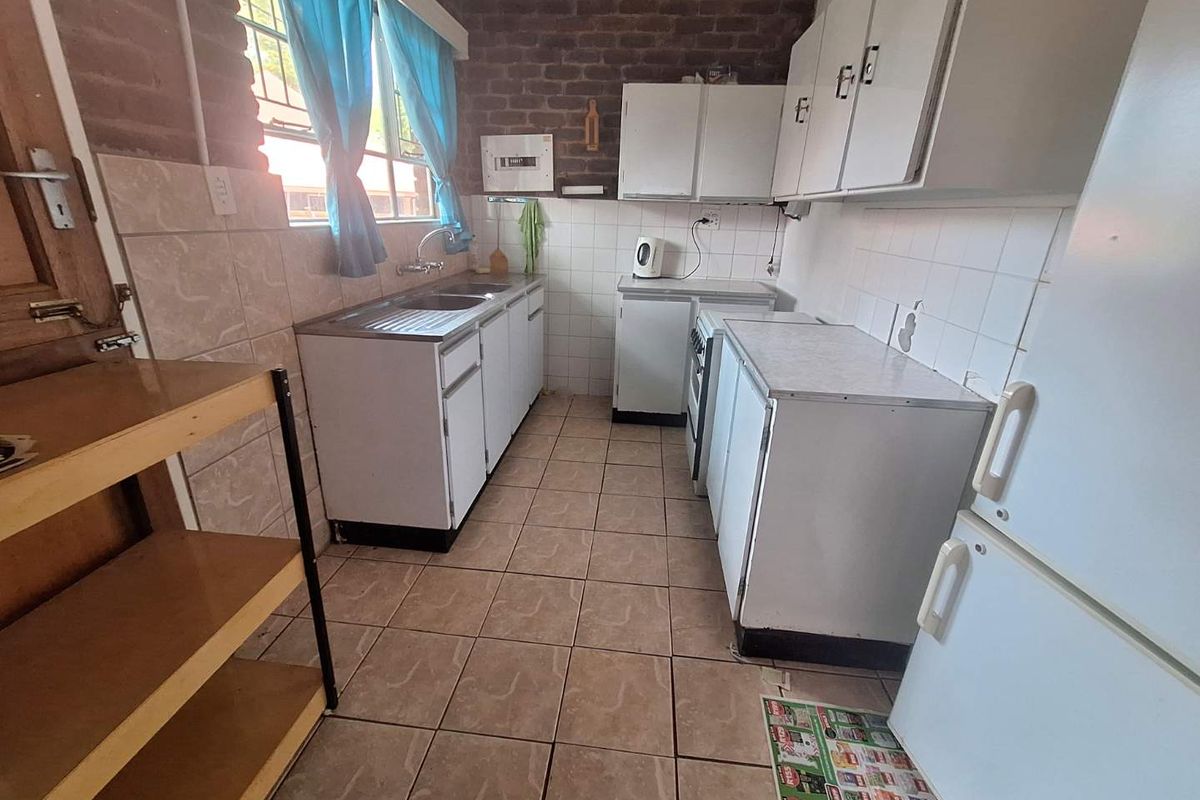 A functional kitchen featuring tiled flooring, exposed brick walls, white cabinetry, and a stainless steel sink unit.