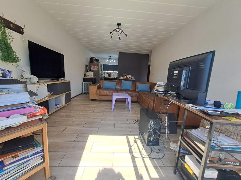 An open-plan living area featuring tiled flooring and a panelled ceiling, providing a functional space that flows into the kitchen area.