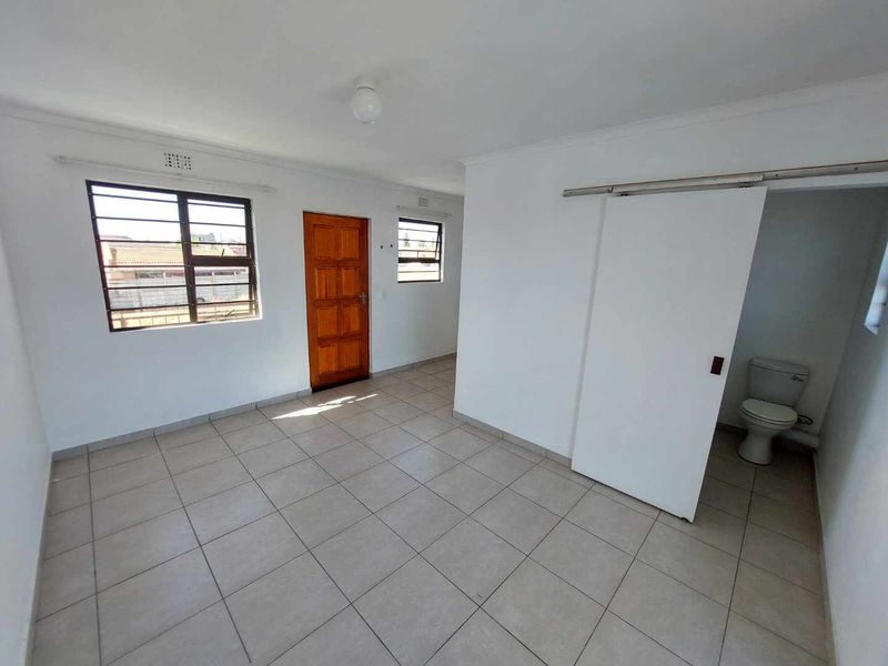 An empty bedroom featuring tiled flooring, burglar bars on windows, and an en-suite bathroom area accessed via a sliding door.