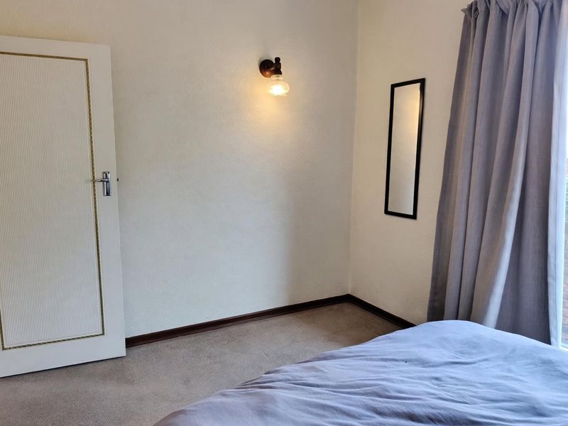 A bedroom featuring neutral walls, carpeted flooring, and a wall-mounted light fixture, offering a clean and functional space.