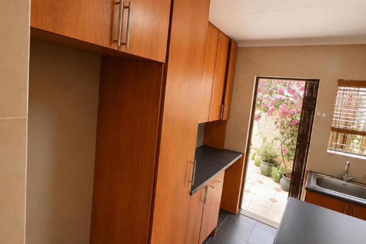 A functional kitchen featuring wood-finish cabinetry, dark countertops, and tiled flooring, with direct access to an outdoor patio area.