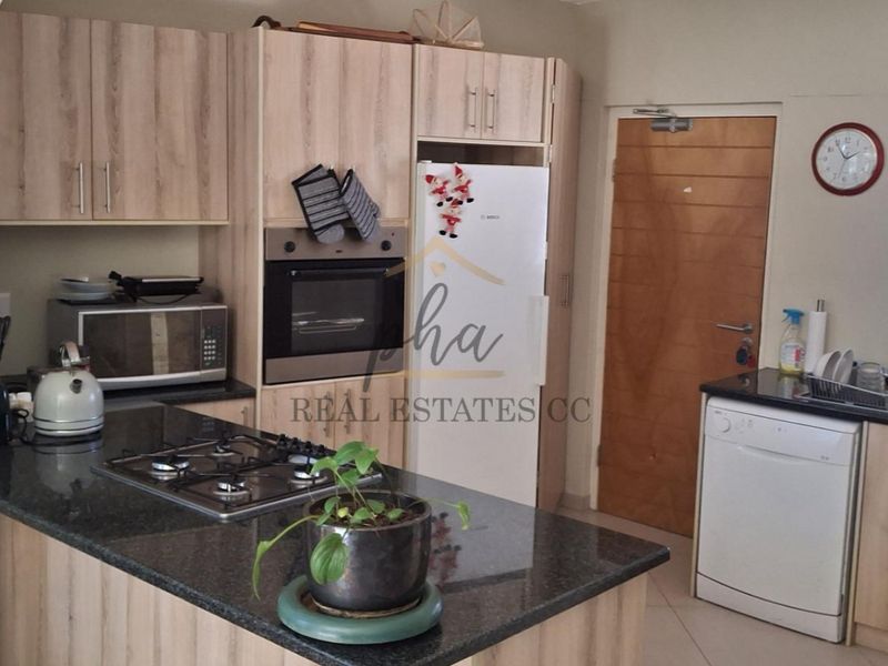 Functional kitchen featuring light wood-finish cabinetry, granite countertops, a gas hob, built-in oven, and a stainless steel sink with a window view.