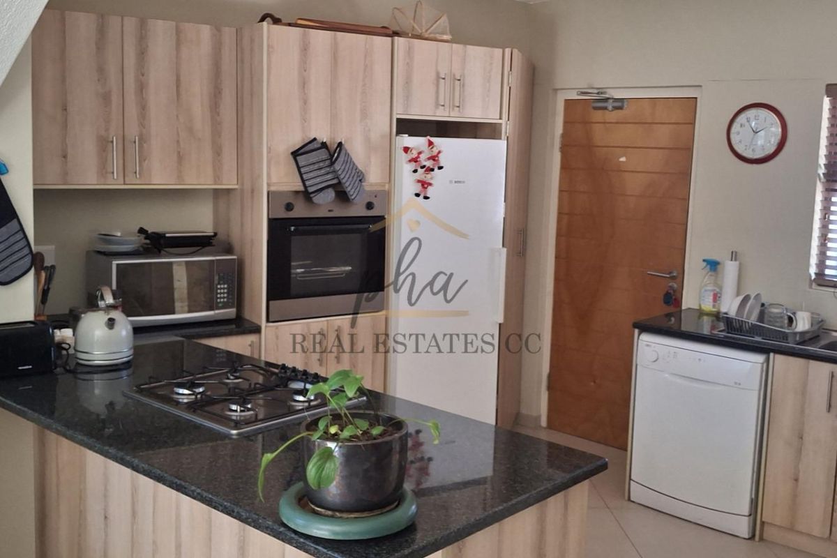 Functional kitchen featuring light wood-finish cabinetry, granite countertops, a gas hob, built-in oven, and a stainless steel sink with a window view.