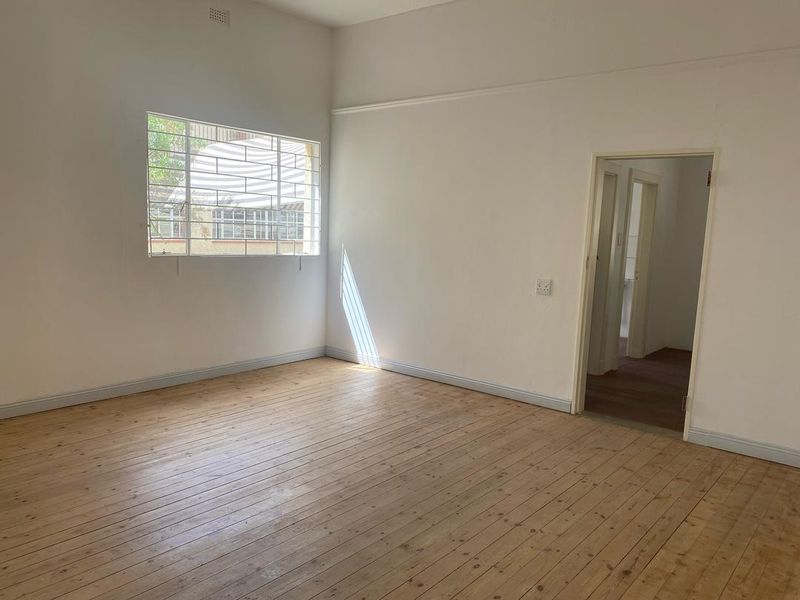 A bright, empty bedroom featuring original timber flooring, a picture rail, and a window fitted with security bars.