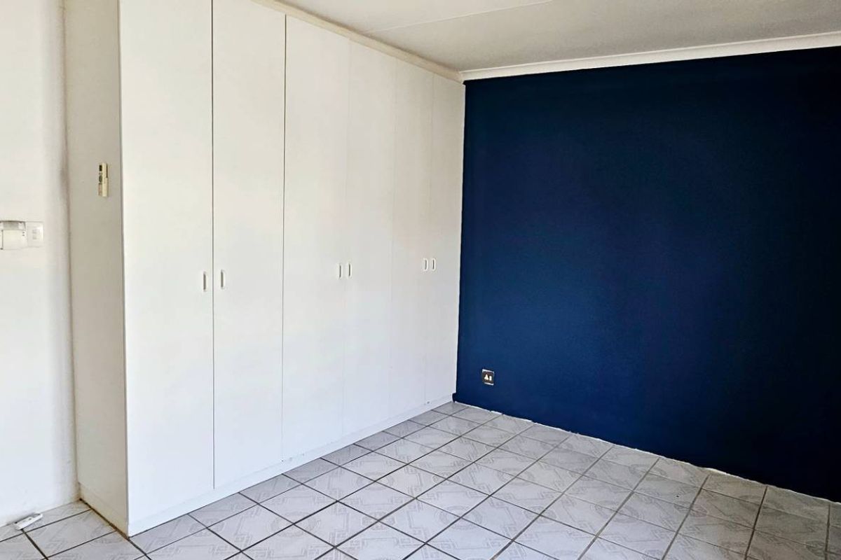 A bedroom featuring built-in wardrobes, tiled flooring, and a dark accent wall, with an adjacent hallway visible through the doorway.