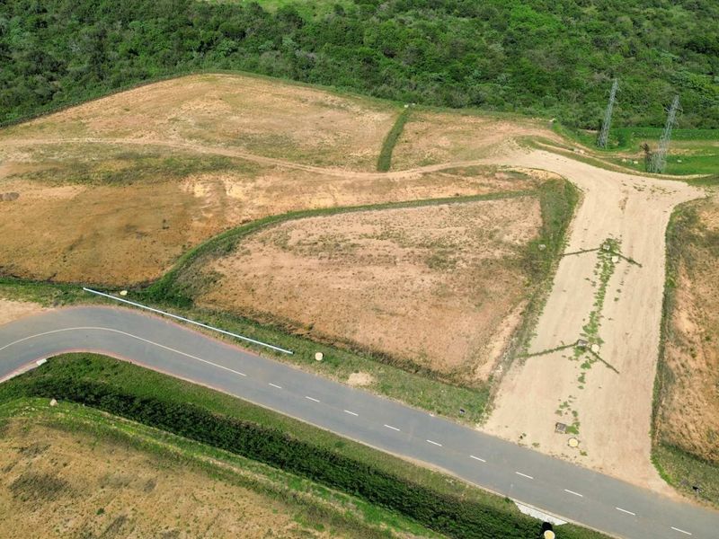 Aerial view of a vacant industrial land plot featuring direct access to a paved road and proximity to power infrastructure.