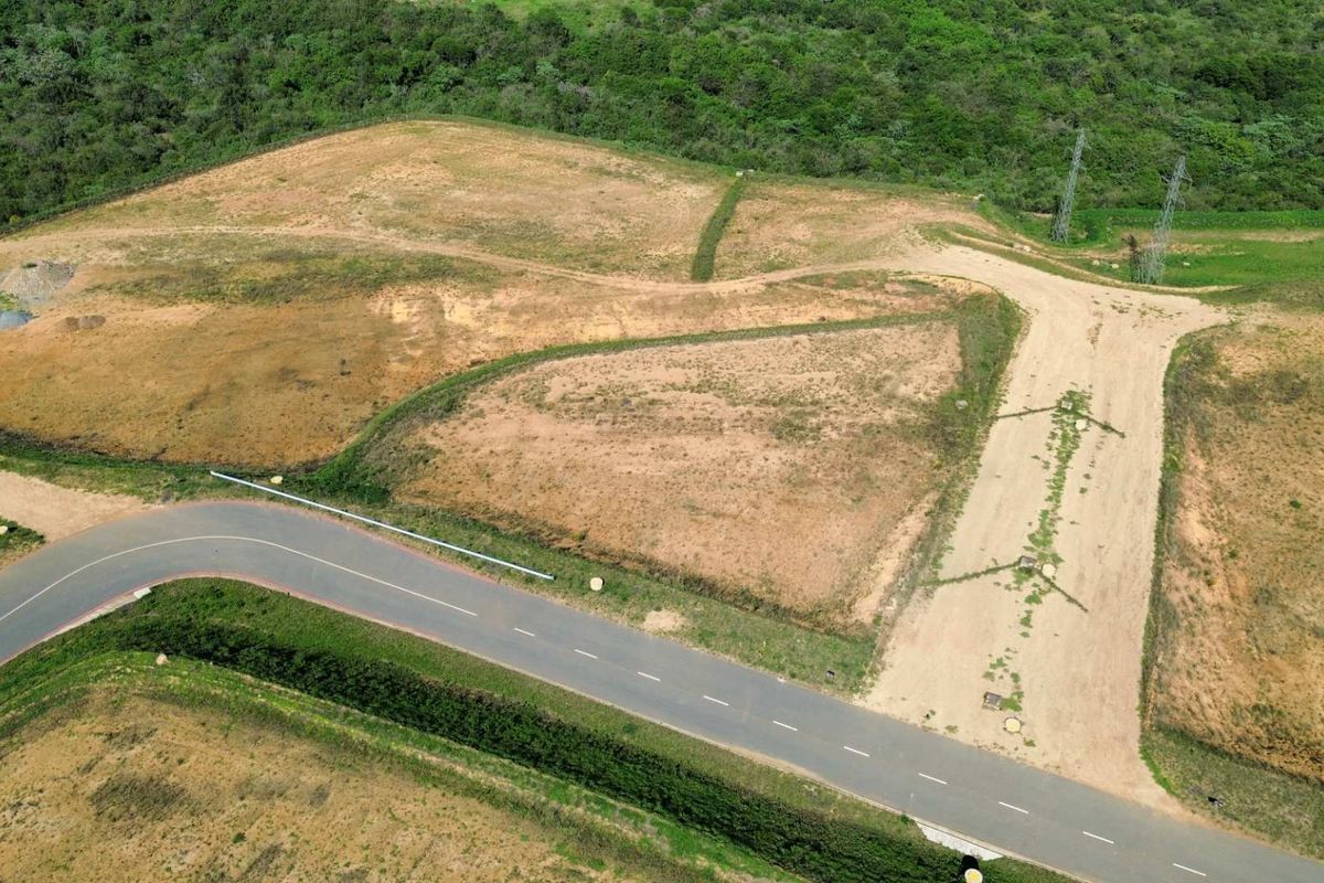 Aerial view of a vacant industrial land plot featuring direct access to a paved road and proximity to power infrastructure.