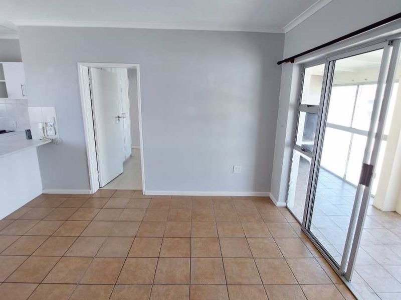 An open-plan living area featuring tiled flooring, neutral walls, and large sliding glass doors leading to an adjacent balcony space.