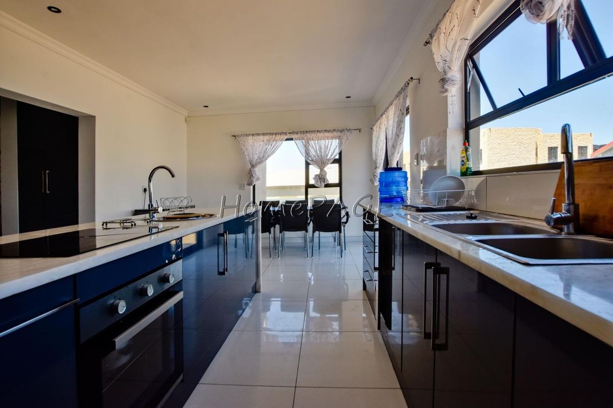 Modern kitchen featuring high-gloss cabinetry, a central island with a built-in oven and hob, double sink, and sleek tiled flooring.