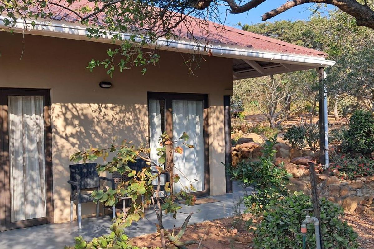 A view of the cottage exterior featuring a covered patio area, glass sliding doors, and a natural landscaped garden setting.