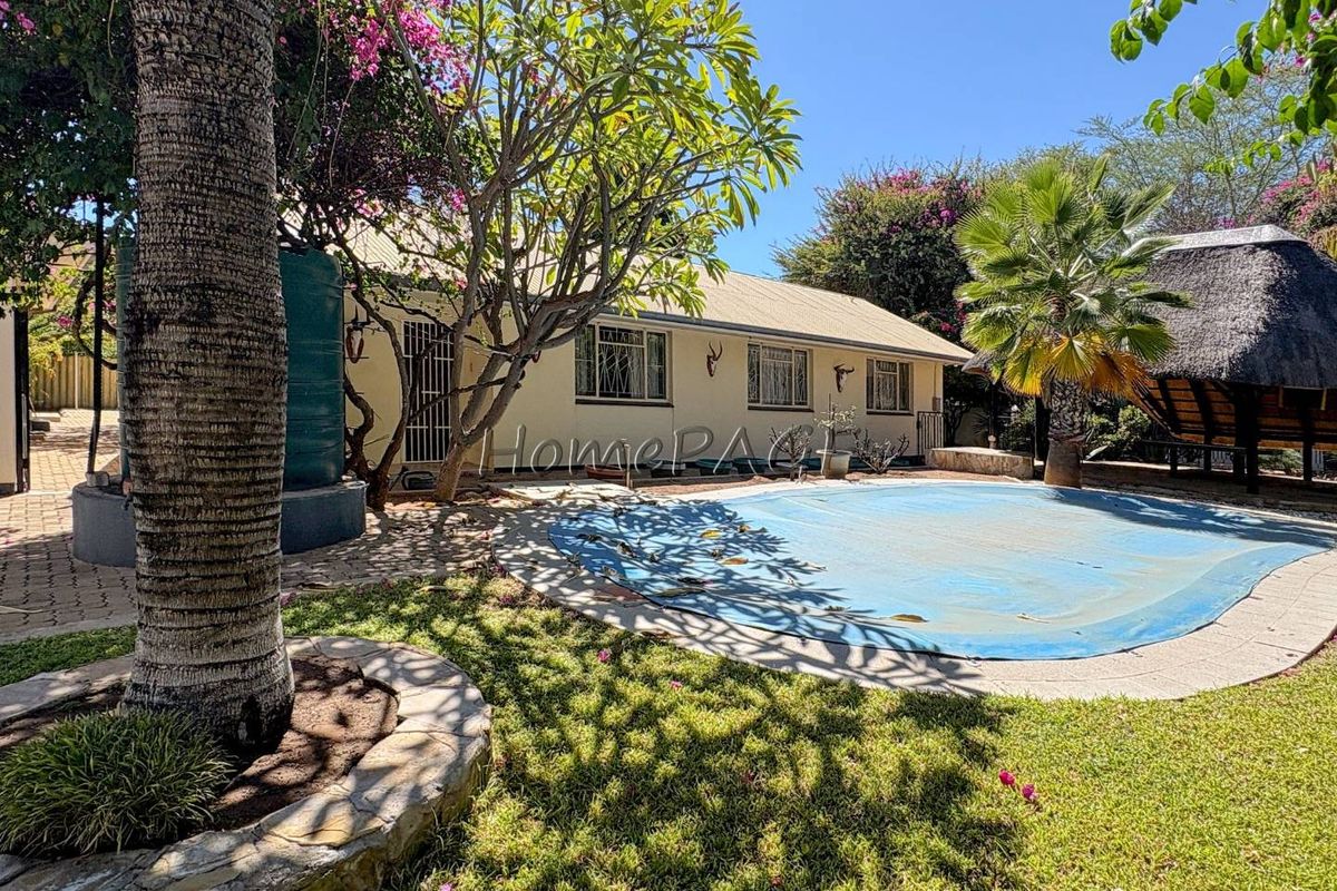 Rear garden featuring a swimming pool with cover, established landscaping, and a thatched lapa area adjacent to the main house structure.