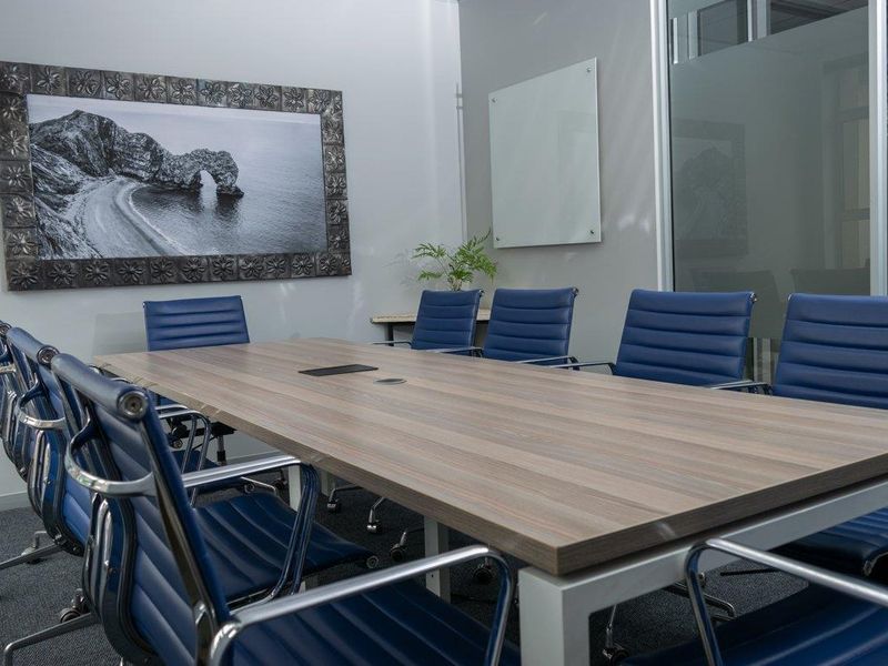 A professional office meeting room featuring a large conference table, glass whiteboard, and modern aluminum-framed glass partitions.
