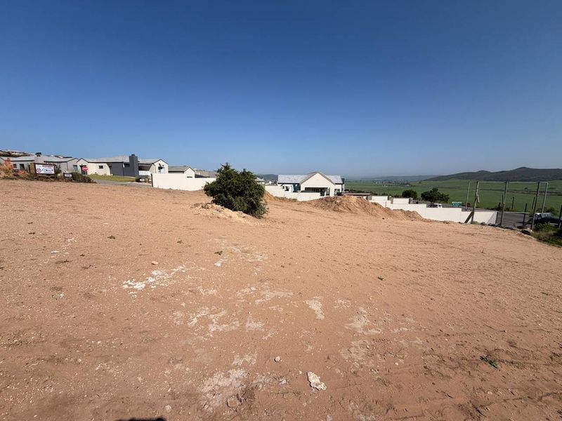 A vacant residential plot with sloped terrain, boundary walls, and surrounding neighborhood views, ready for development.