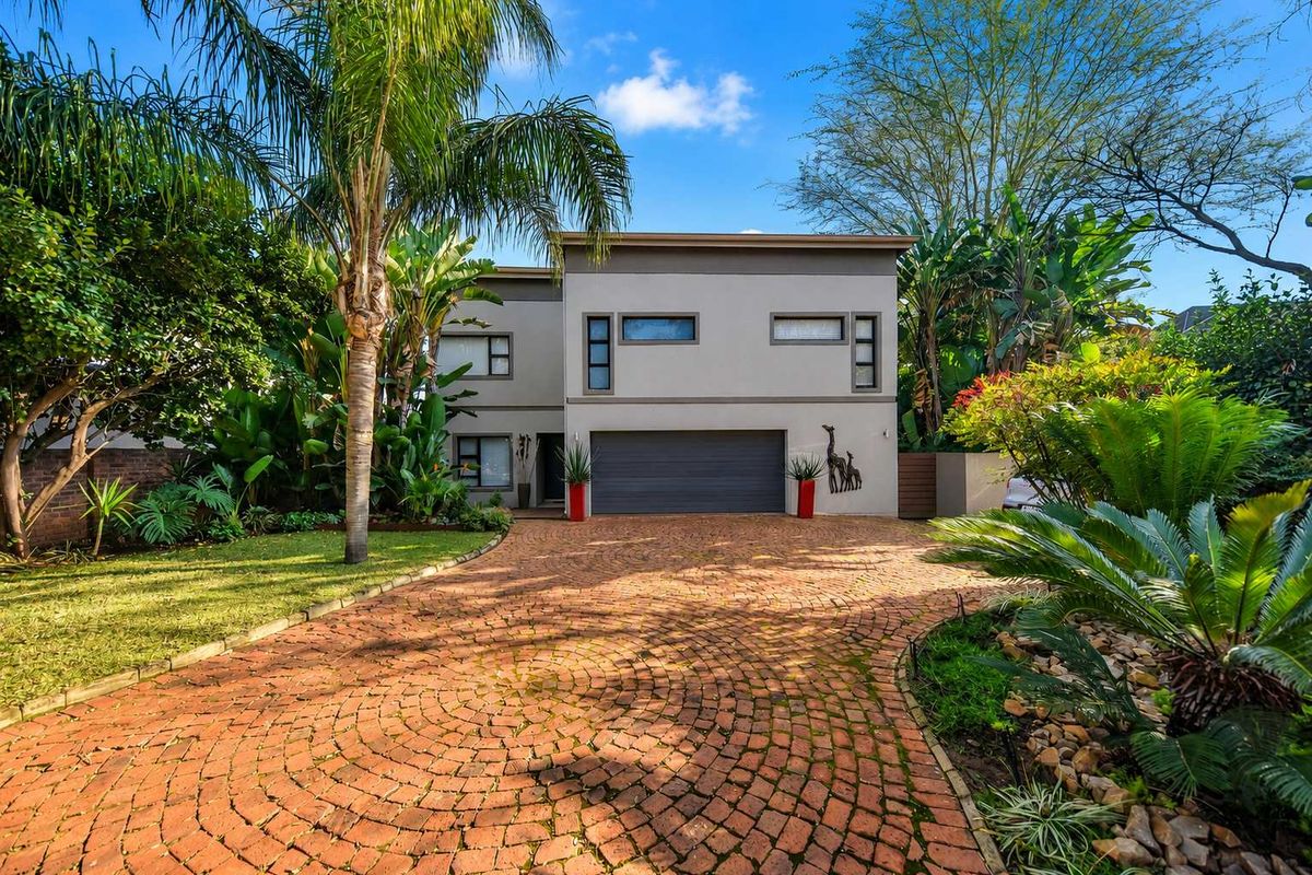 A modern two-story residential property featuring a double garage, a well-maintained brick paved driveway, and lush landscaped gardens.