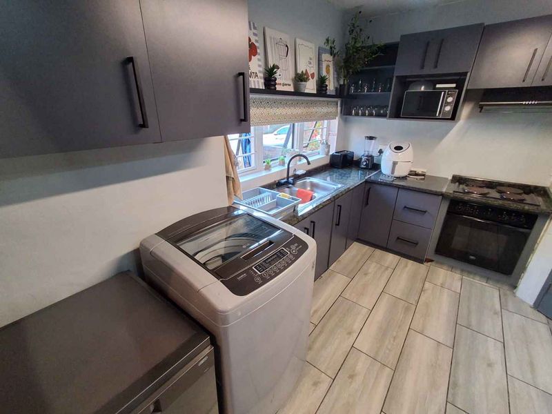 Modern kitchen featuring dark grey cabinetry, laminate countertops, integrated oven and hob, and durable tiled flooring with a functional layout.