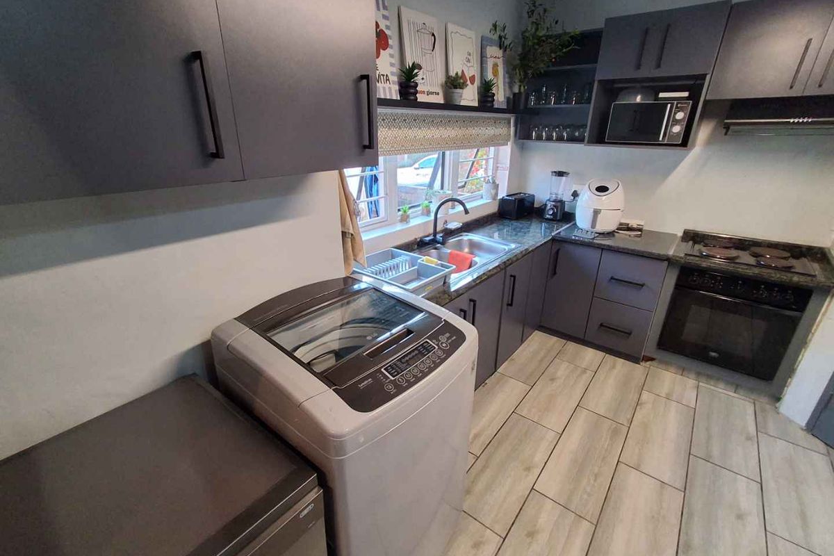 Modern kitchen featuring dark grey cabinetry, laminate countertops, integrated oven and hob, and durable tiled flooring with a functional layout.