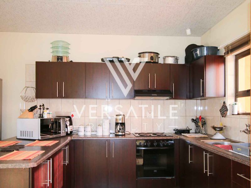 A functional kitchen featuring dark wood cabinetry, laminate countertops, a built-in oven with extractor fan, and a tiled backsplash.