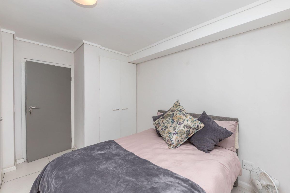 A clean and well-maintained bedroom featuring built-in cupboards, neutral wall finishes, and tiled flooring.
