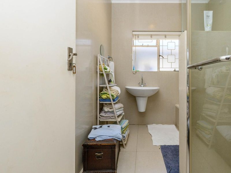 A functional bathroom featuring a pedestal basin, tiled walls and flooring, and a glass-enclosed shower area with security bars on the window.